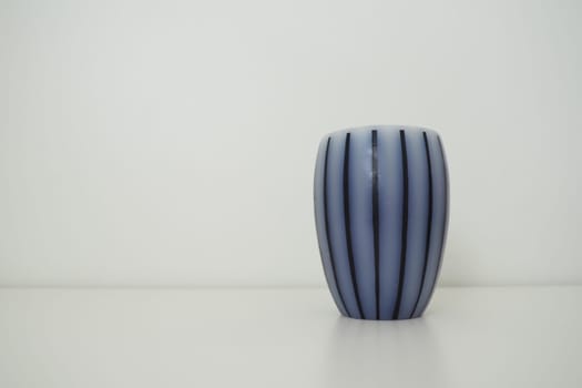 Scented candle on a white surface with a white background behind. Gray striped candle or vase