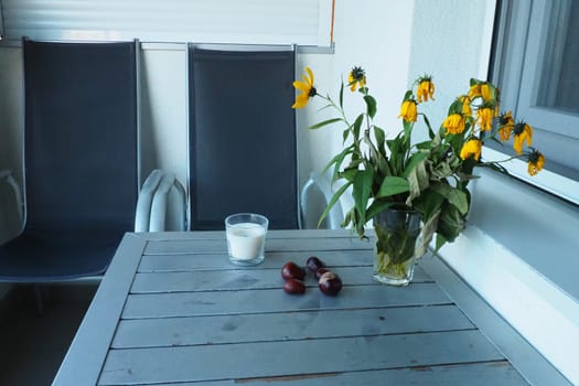 Plants and flowers of Jerusalem artichoke in a vase. Chestnut fruits on the table. Table and chairs on the balcony or terrace. End of season at the hotel. The table is painted silver