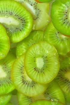 Close-up view of the green kiwi fruit slices in water background. Texture of cooling fruit drink with macro bubbles on the glass wall. Flat design. Vertical image.