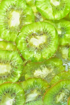 Close-up view of the green kiwi fruit slices in water background. Texture of cooling fruit drink with macro bubbles on the glass wall. Flat design. Vertical image.