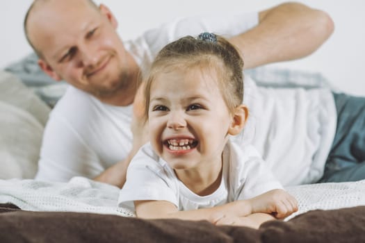 Father plays with little daughter 2-4 on bed. Dad tickles kids feet. Family having fun