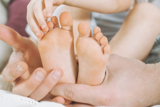 Children's feet in hands of father. Dad tickles feet of kid. Baby counts toes