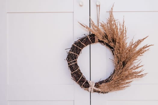 Dry herbal twig, tightly woven wreath with twisted cereal and white lace ribbon. White background. Traditional seasonal ethnic holiday decoration. Unique design greeting symbol on door. Copy space