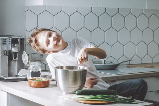 Boy 7-10 smiles and whips omelet with whisk in kitchen. Son, doing household chores.