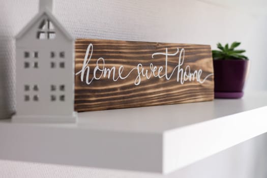 Decorative sign house sweet home from a burnt tree on a white shelf with a toy house and a flower pot, selective focus