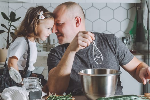 Father whips omelet with whisk, playing with daughter. Man doing household chores.