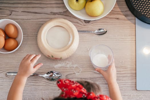 Hands of little girl in red headband bake apple pie in kitchen. Child puts sugar in measuring cup. Children help on household chores. Kid cooking food. Top view