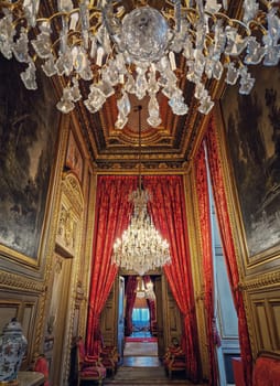 Beautiful decorated Napoleon apartments at Louvre palace. Royal family rooms with cardinal red curtains, golden ornate walls, paintings and crystal chandeliers suspended from ceiling