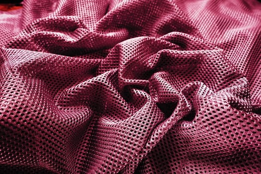 Synthetic fabric with holes, laid in waves and twisted into folds. Beautiful drape. Fabric for curtains, interior design, and decor. Twisted or wrinkled red burgundy porous fabric.