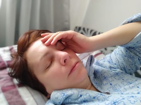 Sick woman in bed. Headache, runny nose and cold. Paleness of the face and faintness of the body. Feeling unwell. The patient holds his forehead with his hand and covers his eyes.