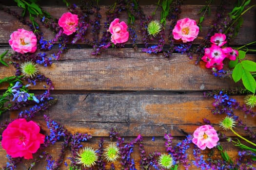 Flowers in a circle on a wooden background. Postcard for the holiday. Roses, geraniums, lavender, sage and hairy chestnuts are placed along the edges on dark boards. Background copy space, flat lay