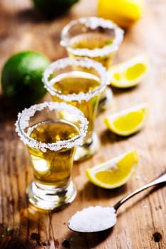Golden mexican tequila in shot glass with lime and salt on vintage wooden table. Nightlife cocktail drinks menu. Closeup of alcohol beverage in pub.