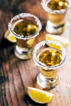 Golden mexican tequila in shot glass with lime and salt on vintage wooden table. Nightlife cocktail drinks menu. Closeup of alcohol beverage in pub.