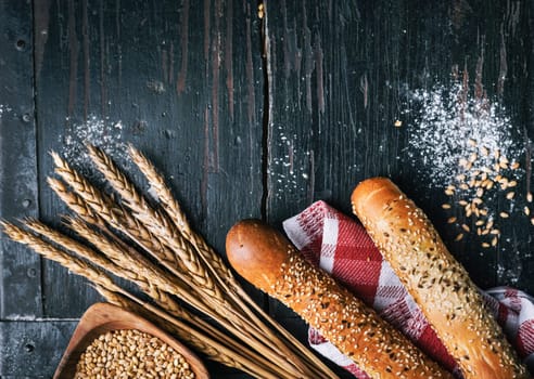 Fresh french baguette bread, organic flour and wholegrain wheat on dark vintage wooden board form above. Top view of traditional baked bread. Bakery shop menu background.
