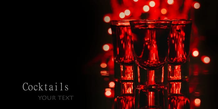 Red alcohol cocktails in shot glasses over red bokeh light and black background. Shots on bar counter in night club party.