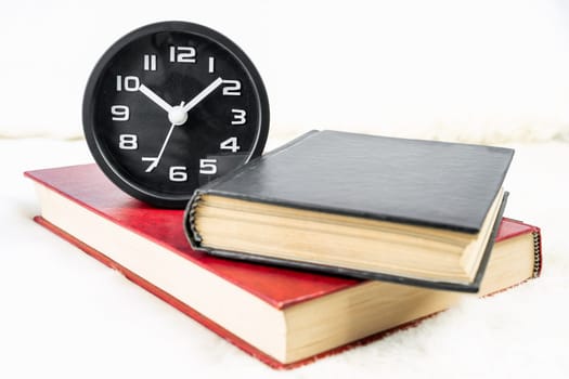 Close up Black alarm clock and book stacked on table