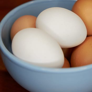 fresh brown and white eggs in a bowl on a kitchen table
