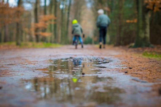 Out of focus scene with mother hiking and kid on a bike in the nature of the forest