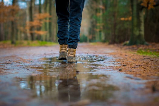 Selective focus shot of hiking boots walking through a puddle of water on a trail in the forest.