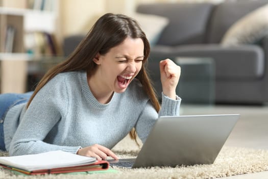 Excited student lying on the floor checking laptop at home