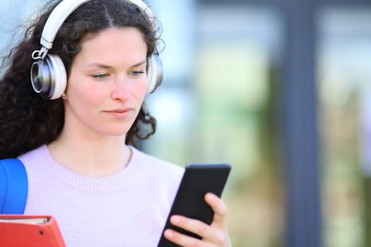 Serious student wearing headphones checking audio on smart phone in the street