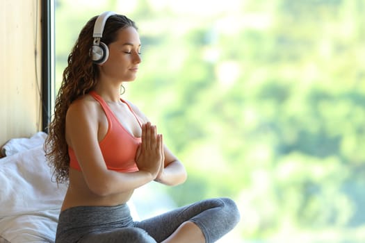 Yogi with headphones listening yoga audio guide at home near a window