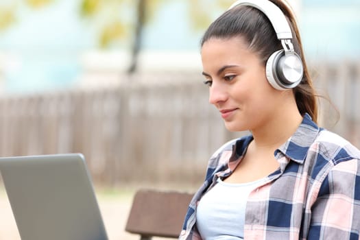 Teen wearing headphones watching videos on laptop in a bench