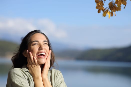 Surprised happy woman looking above in a lake on holiday with copy space