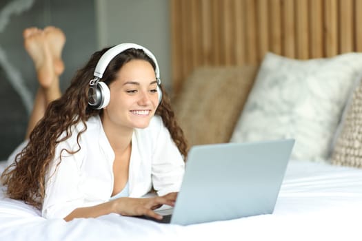 Woman with headphones checking laptop on a bed in the bedroom