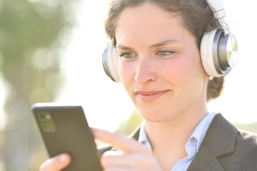 Businesswoman wearing headphones listening audio and checking phone