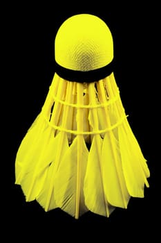 a yellow shuttlecock with feathers on the black background