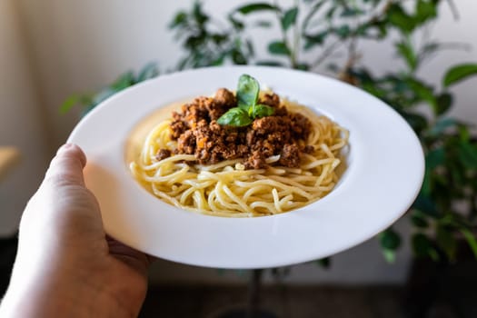 Plate with classic Italian pasta spaghetti bolognese in hand.