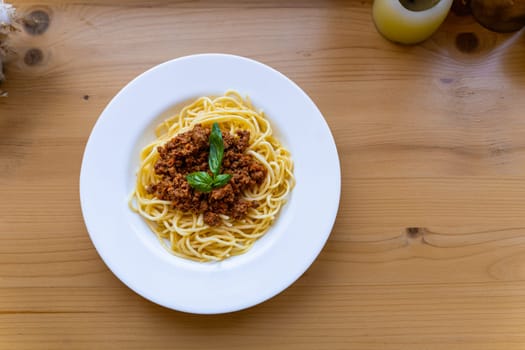 Spaghetti bolognese in a white plate, decorated with basil leaf on a wooden table, View from above. A classic dish of Italian cuisine.