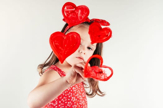 Pretty little girl carefully draw red hearts with paintbrush on invisible wall. Portrait of child on white. Drawing, creative present. Saint Valentine's Day concept, holiday of all lovers.