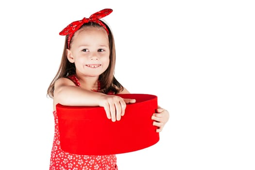 Happy little girl with smile hold big red present box. Portrait of child isolated on white. Joyful kid in festive red outfit. Saint Valentine's Day concept, holiday of all lovers, celebration.