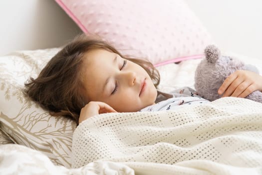 Cute little girl sleeping on bed under blanket with teddy bear. Portrait of asleep child. Morning, have sweet dream. Sleep with favorite stuffed toy. Resting in bedroom, cozy interior.