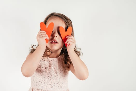 Beautiful little girl close eyes with red heart shaped greeting card. Portrait of child on white. Paper cut valentine, handmade present. Saint Valentine's Day concept, holiday of all lovers.