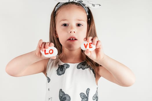 Charming little girl hold decorative stone halves with letters LOVE. Portrait of child on white. Handmade gift for holiday, creative craft. Saint Valentine's Day concept, holiday of all lovers.