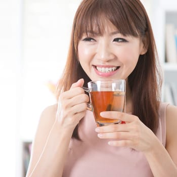 Portrait of happy Asian girl enjoying cup of hot tea in the morning. Young woman indoors living lifestyle at home.
