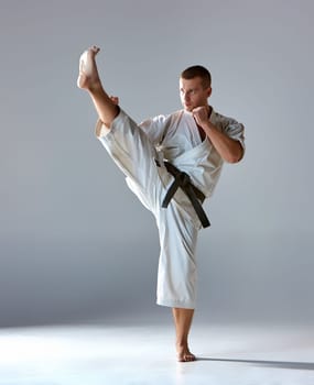Man in white kimono and black belt training karate over gray background.