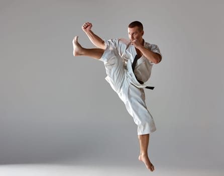 Man in white kimono and black belt training karate over gray background.
