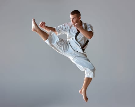Man in white kimono and black belt training karate over gray background.