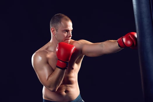 Young boxer in red gloves boxing over black background