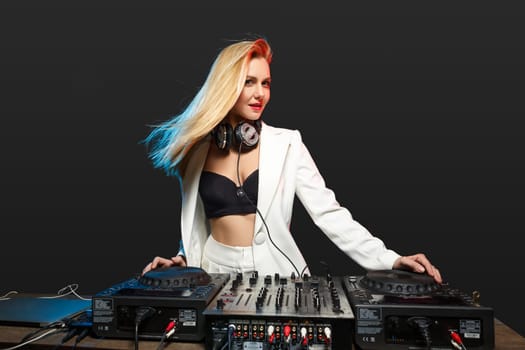 Beautiful blonde DJ girl in a white suit on decks on the party on the black background