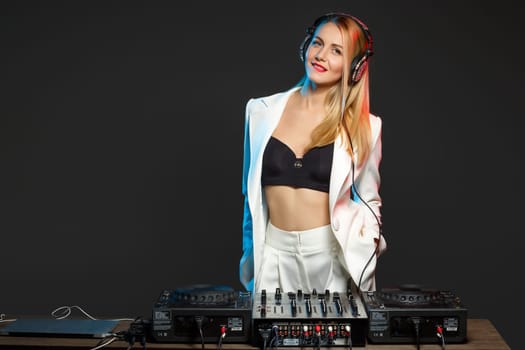 Beautiful blonde DJ girl in a white suit on decks on the party on the black background
