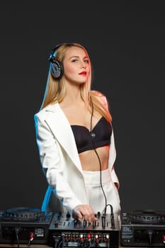 Beautiful blonde DJ girl in a white suit on decks on the party on the black background