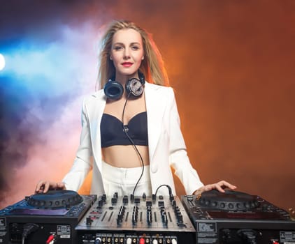 Beautiful blonde DJ girl on decks on the party on the background of orange smoke