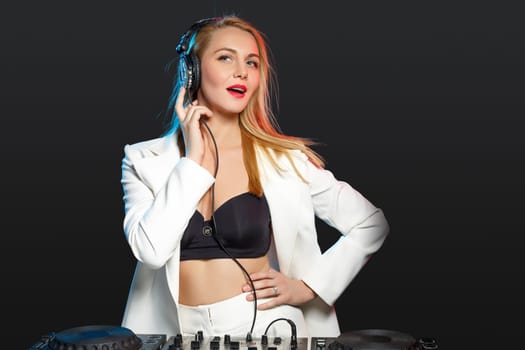 Beautiful blonde DJ girl in a white suit on decks on the party on the black background