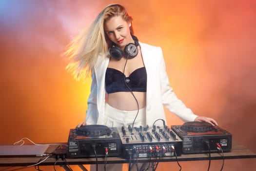 Beautiful blonde DJ girl on decks on the party on the background of orange smoke