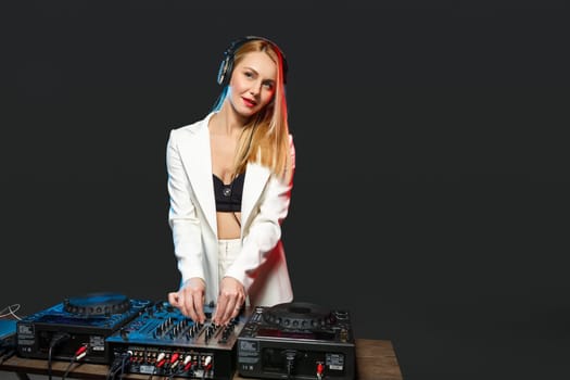 Beautiful blonde DJ girl in a white suit on decks on the party on the black background